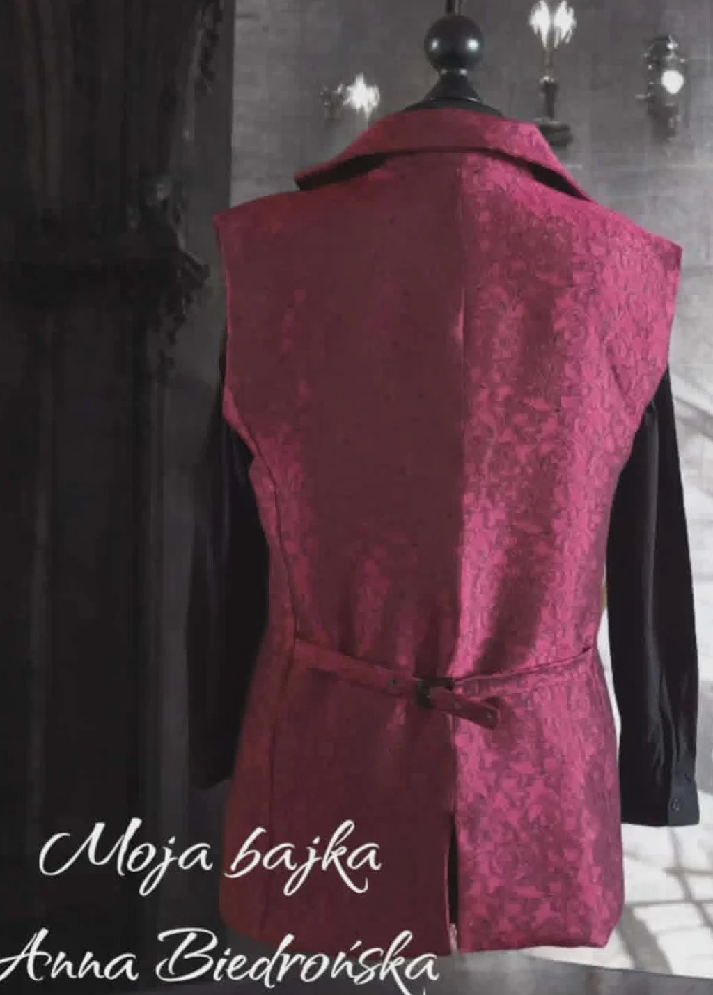 Burgundy velvet vest displayed on a mannequin with black long sleeves and vintage street lamps in background