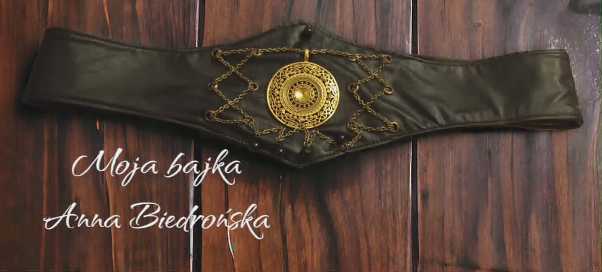 Black leather belt with ornate gold circular buckle on wooden surface with handwritten names