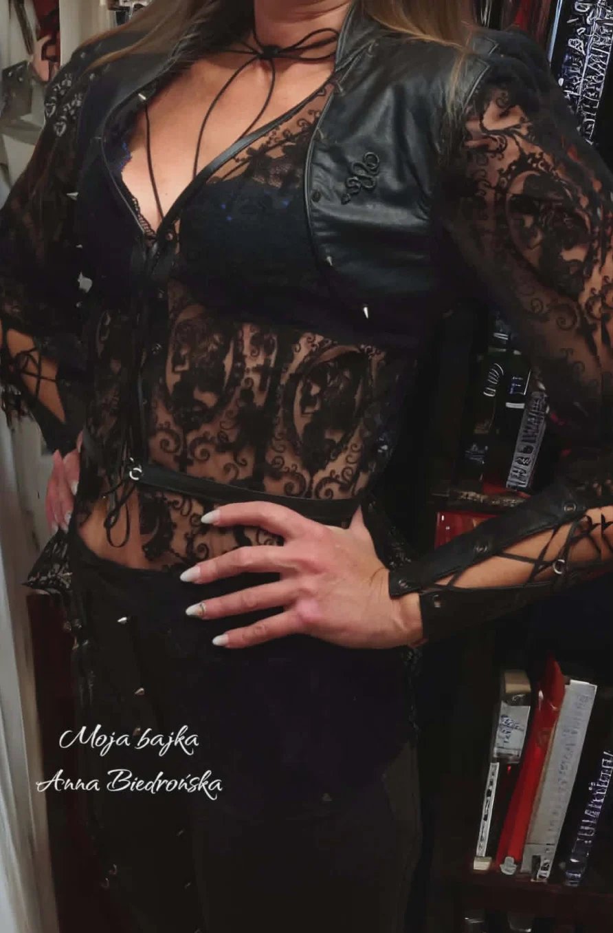 Woman wearing black leather jacket and lace corset top with choker against retail backdrop