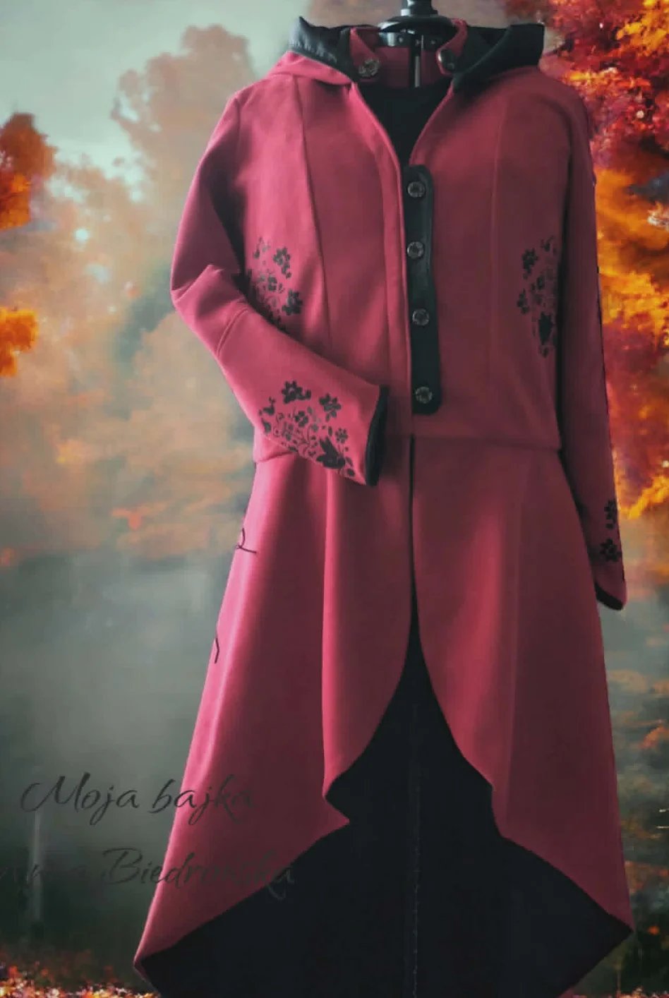 Mannequin wearing pink asymmetrical coat with floral embroidery over black garment against fiery background