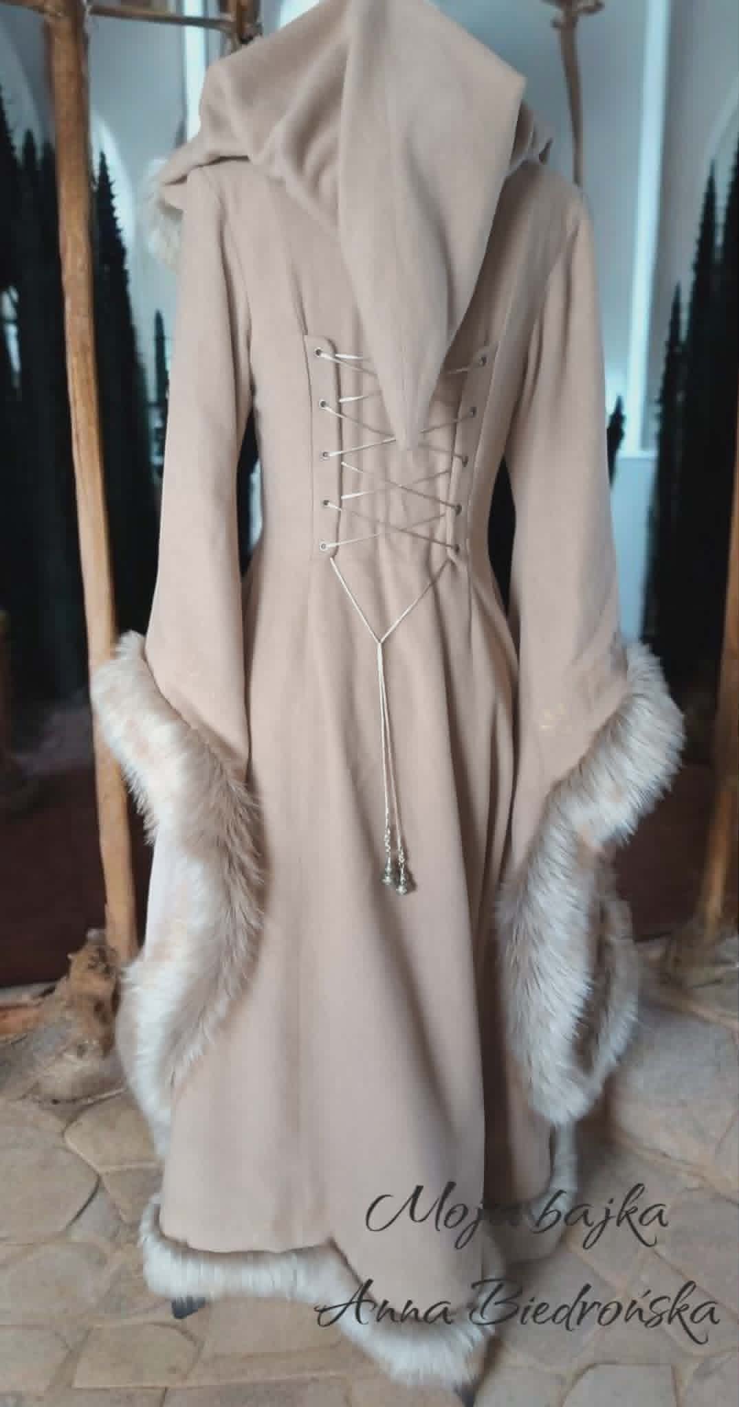 Beige medieval-style cloak displayed on a dress form, featuring lace-up back detail and white fur trim at the hem