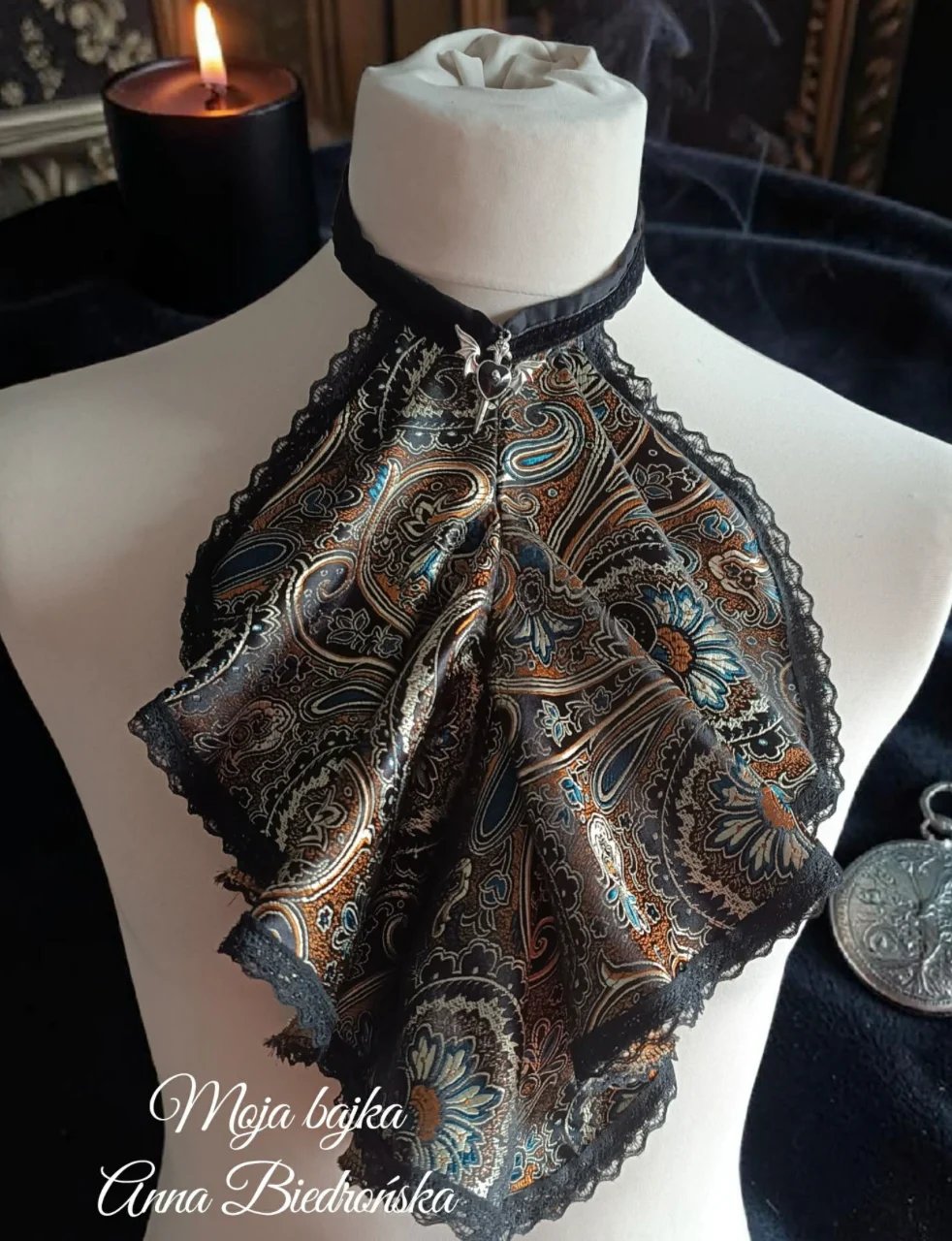 Ornate black and gold paisley shawl draped on white dress form mannequin with candles in background