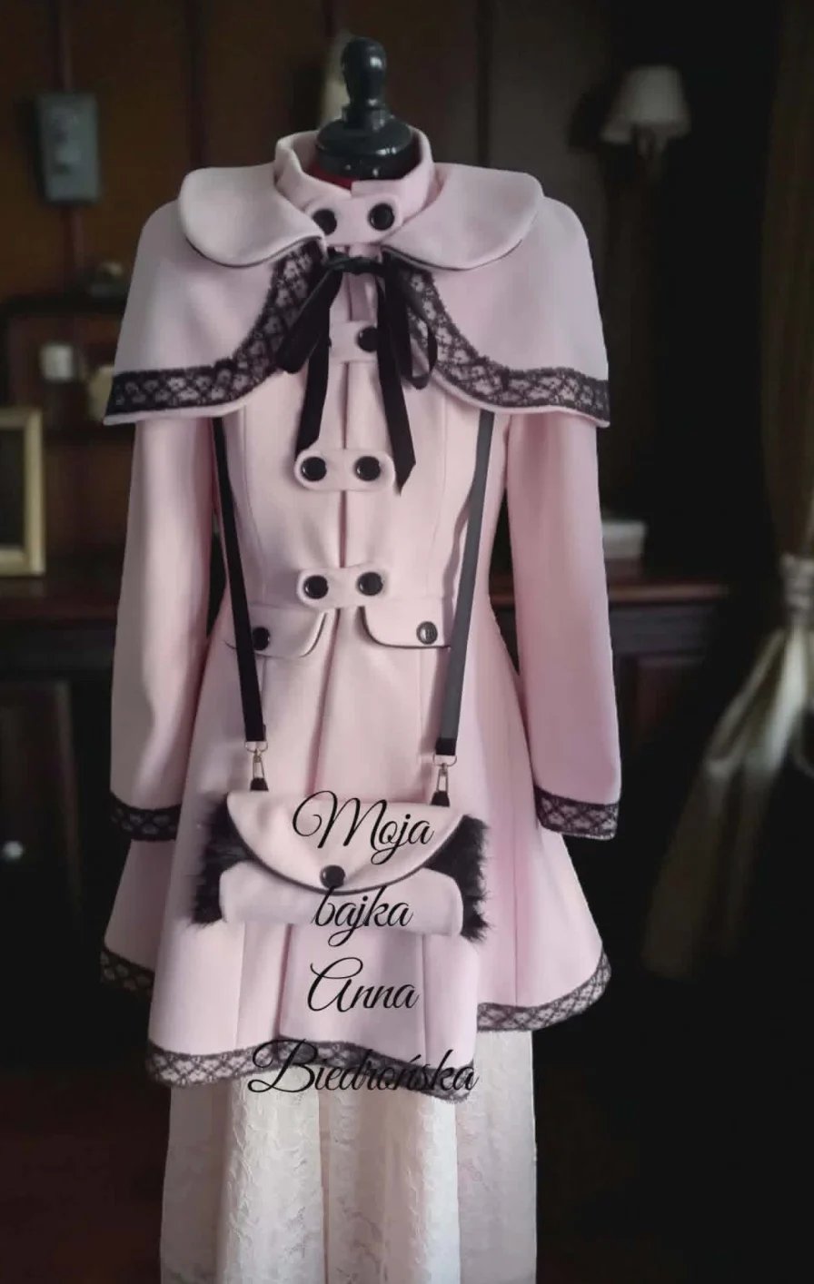 Pale pink vintage-style dress on mannequin with black lace trim, cape collar, and decorative buttons displayed indoors