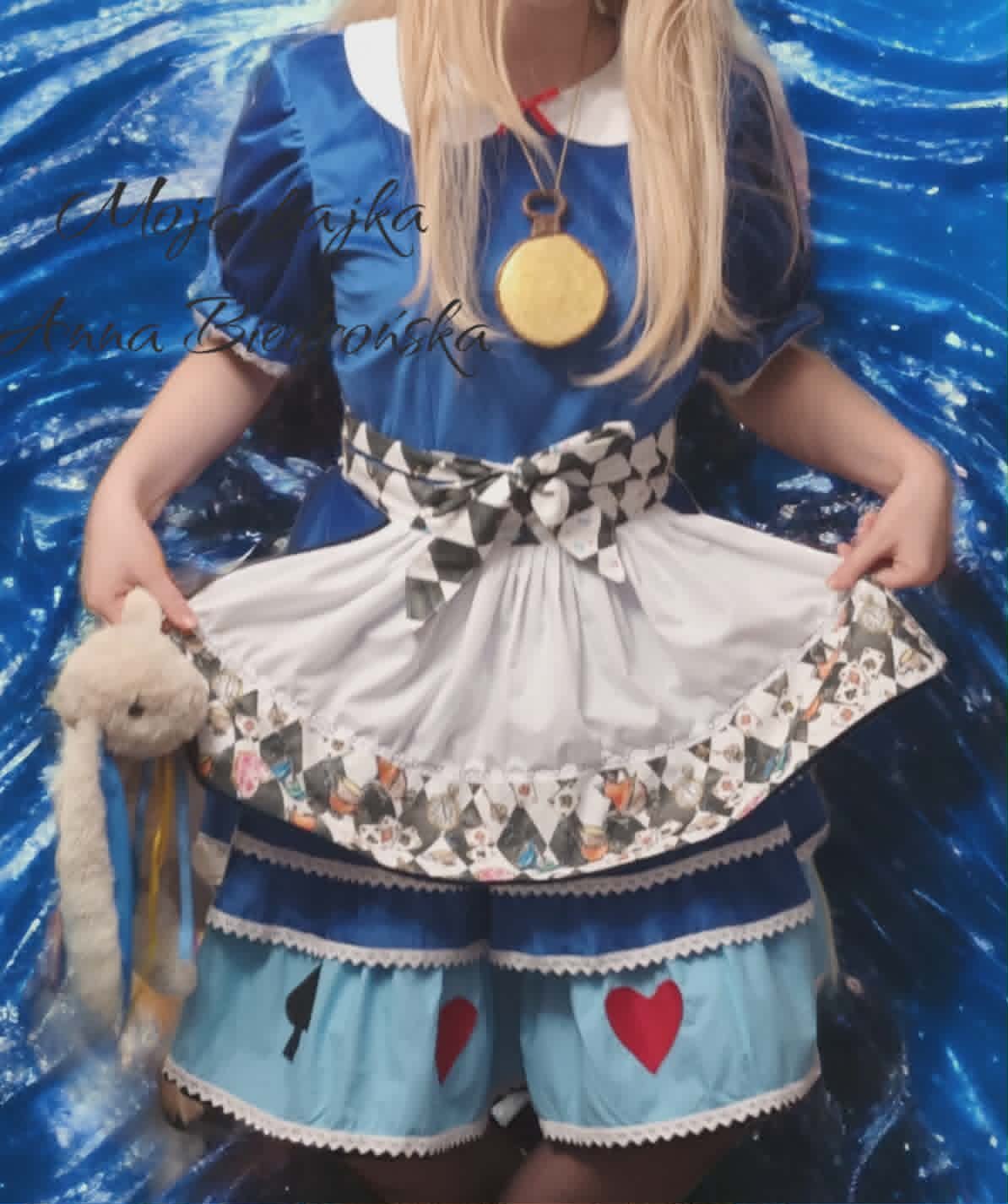 Person wearing an anime-inspired outfit with layered skirts and a gold medal necklace against a blue background