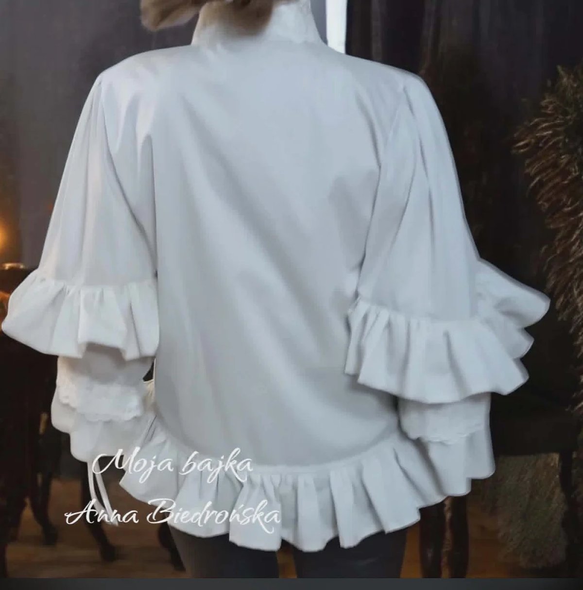 Back view of a woman wearing a white blouse with ruffled three-quarter sleeves and hemline
