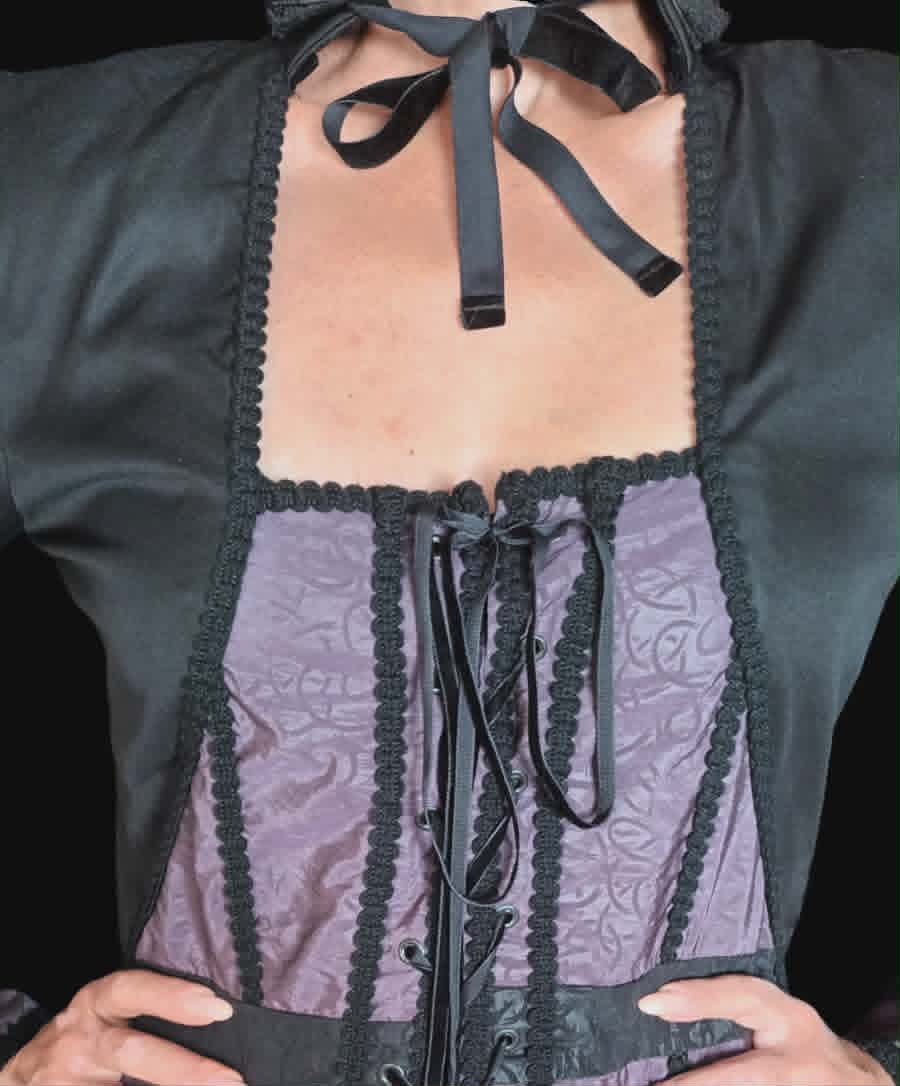Person wearing a black corset-style vest with purple patterned panels and black ribbon ties held up at chest level