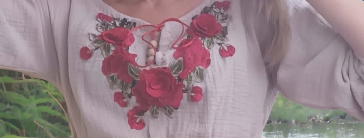 Close-up of a white linen shirt with a decorative embroidered neckline featuring red roses and green leaves