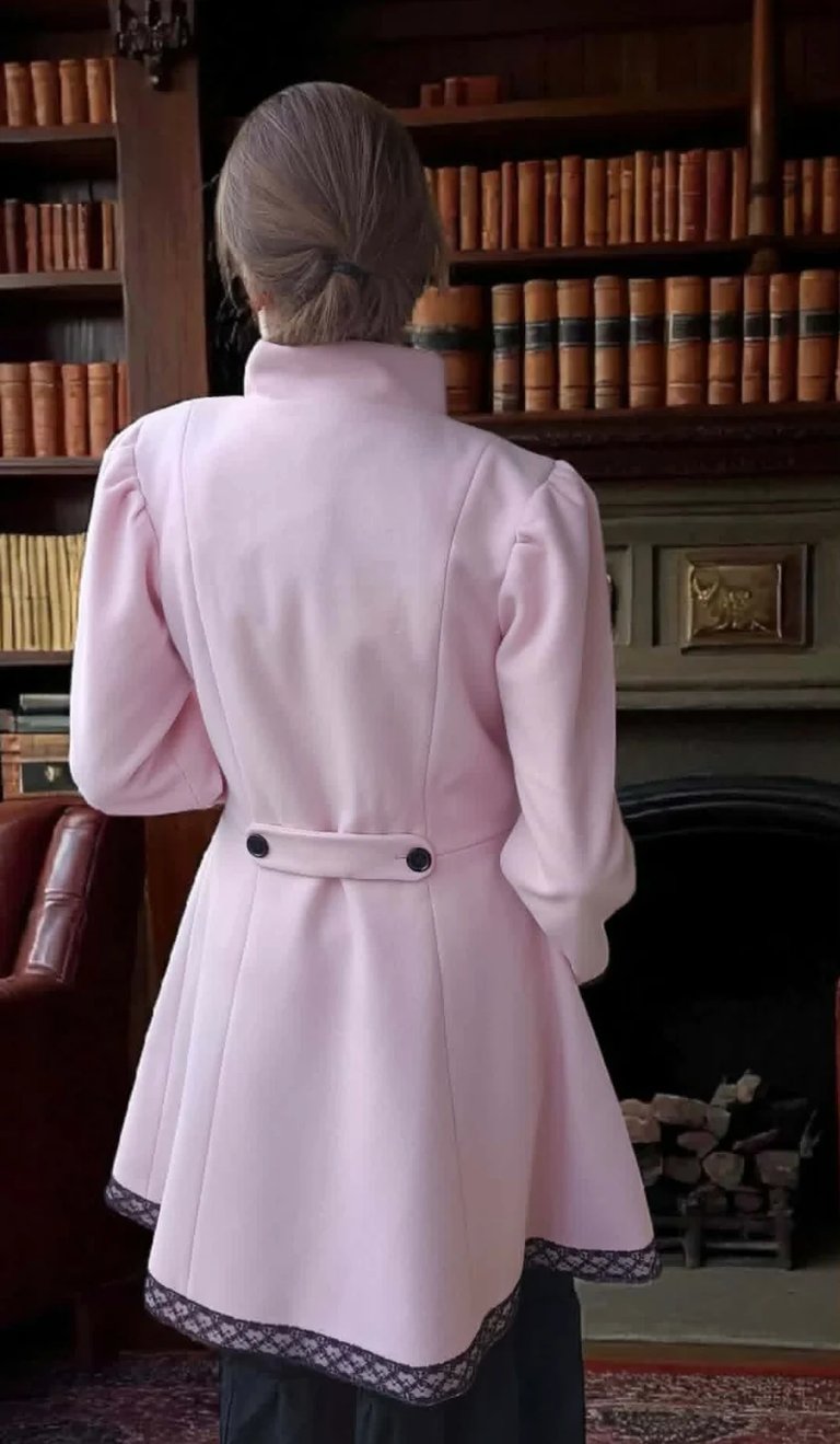 Woman from behind wearing pink coat with gray hair in library setting with bookshelves and fireplace