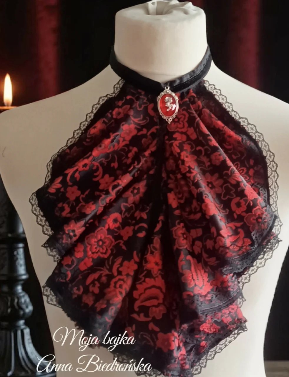 Red damask lace choker with black lace trim and ornate pendant on mannequin bust against dark background