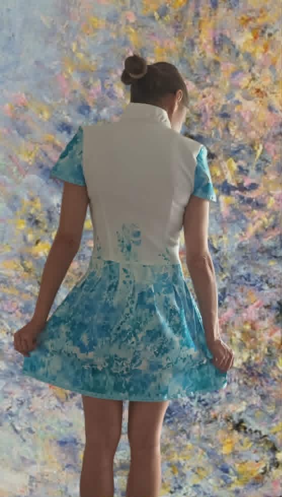 Woman from behind wearing white sleeveless vest and blue patterned skirt standing in front of colorful abstract painting