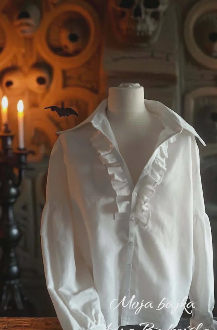 White ruffled blouse on a dress form with Halloween decorations including orange jack-o-lantern backdrop and lit candles in background