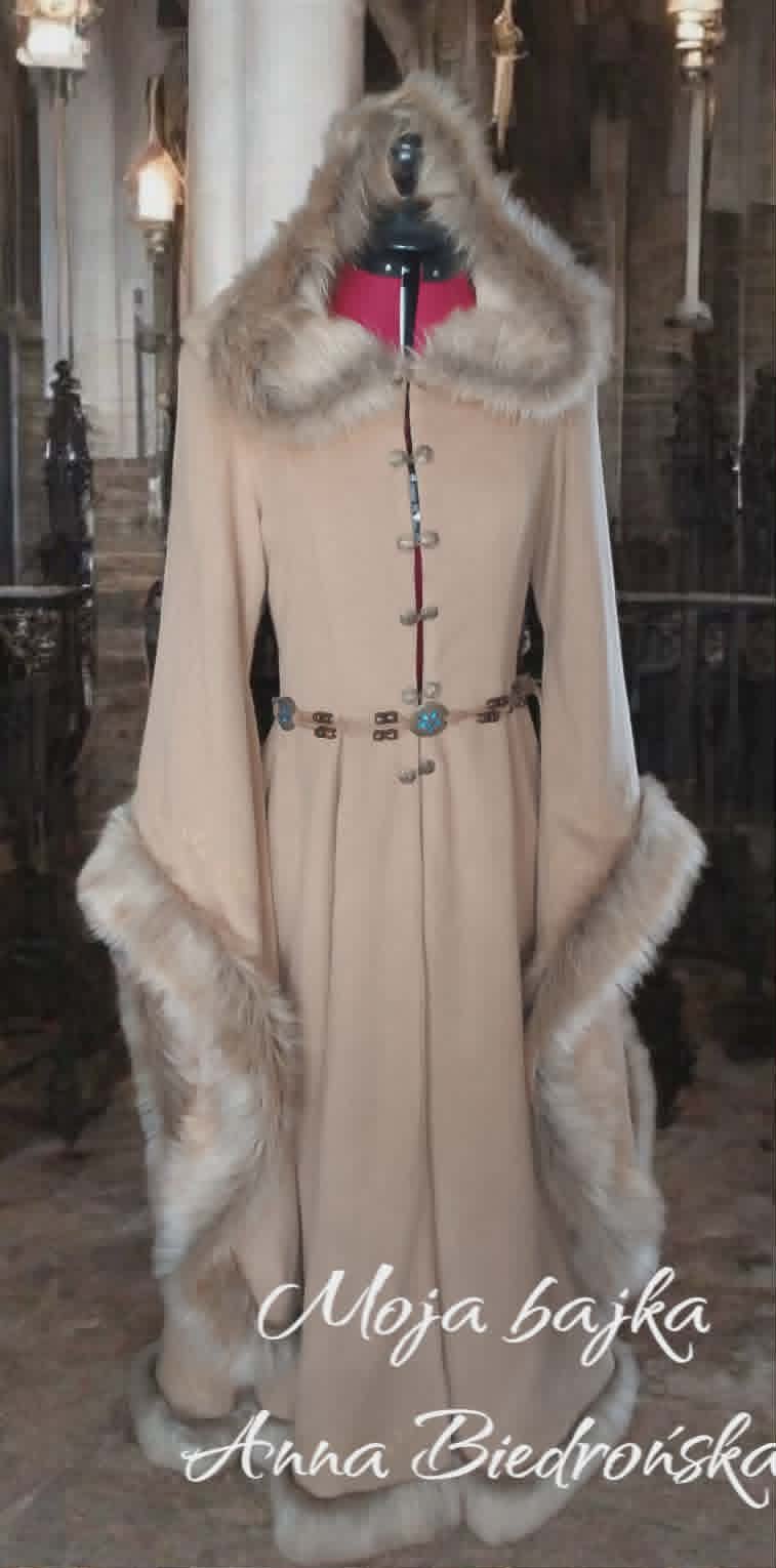 Elegant beige floor-length coat on dress form with fur collar and hem, red belt accent, displayed in gallery setting