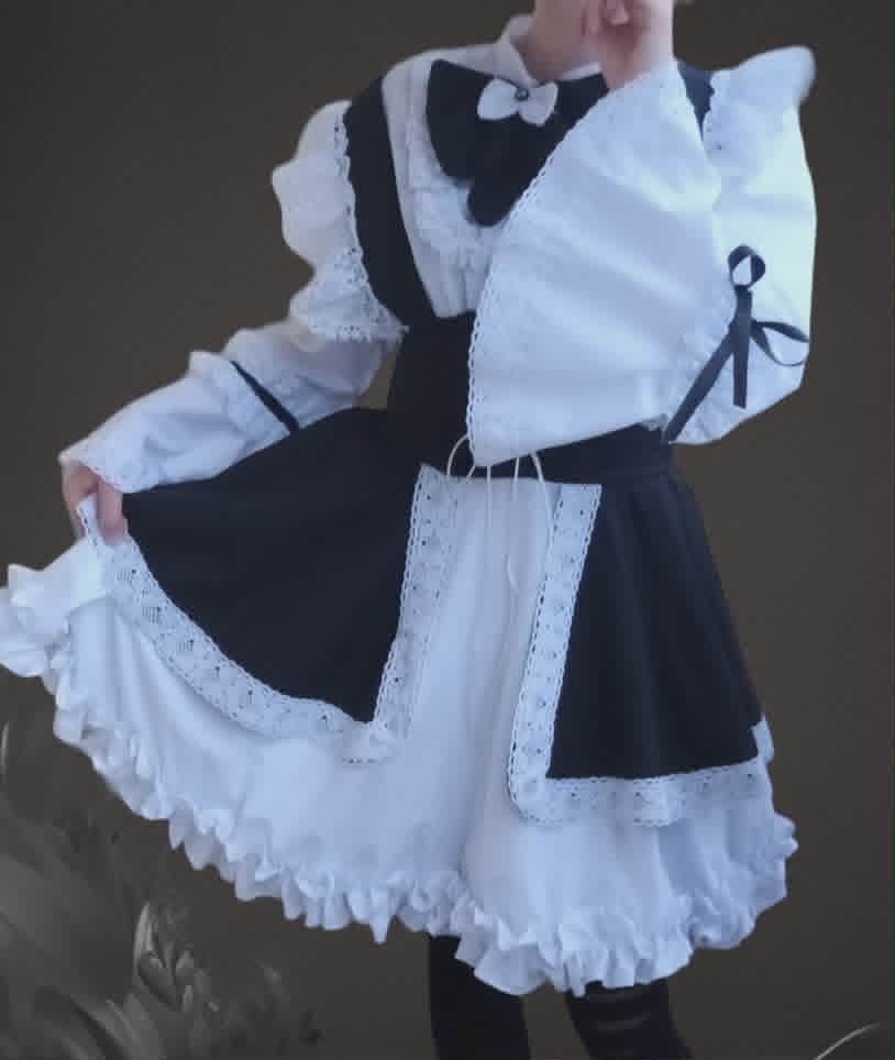 Person wearing a black and white maid costume with ruffled apron, puffed sleeves, and a bow tie