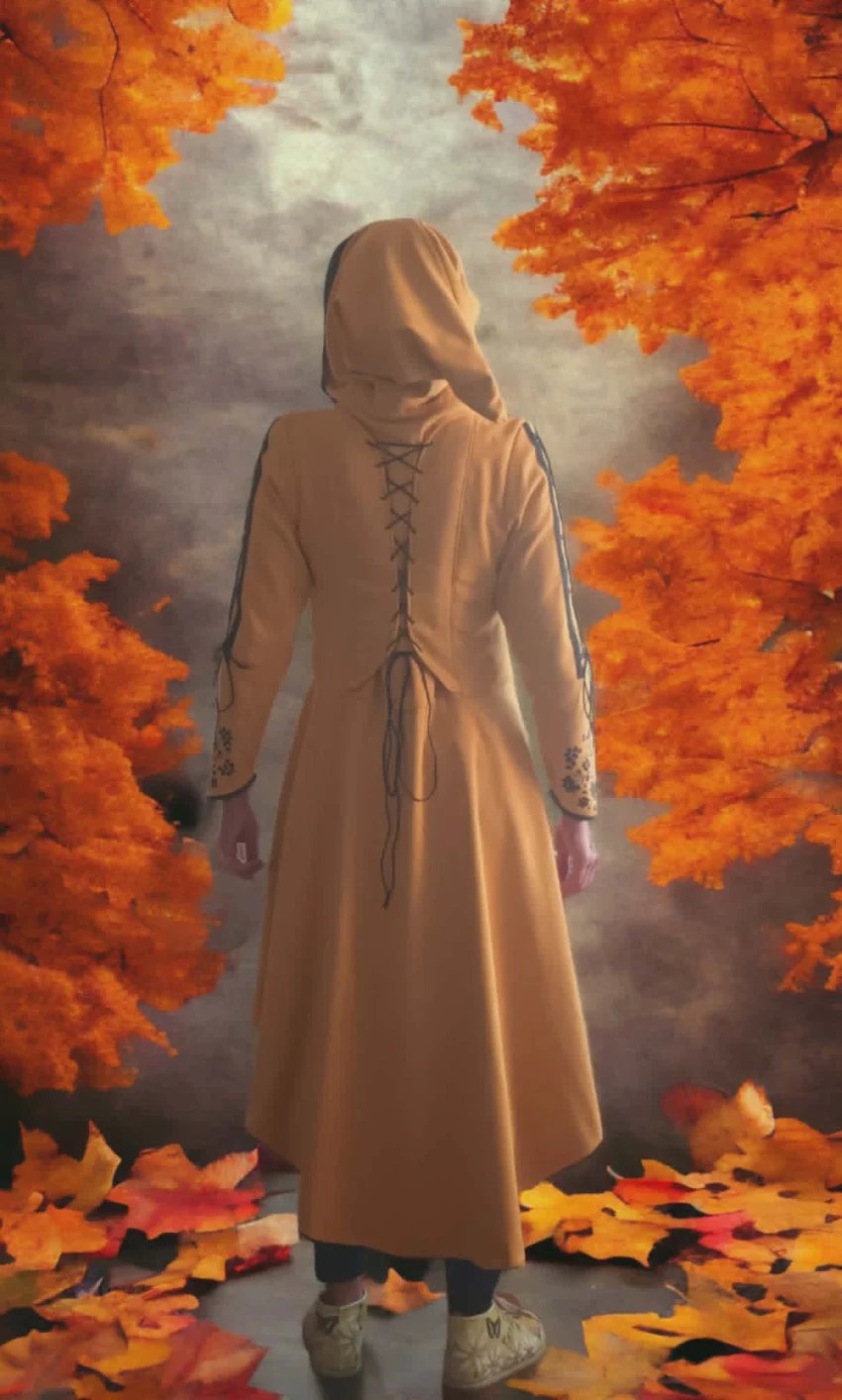 Person wearing a beige lace-back dress and hood standing among vibrant orange autumn leaves against a cloudy sky