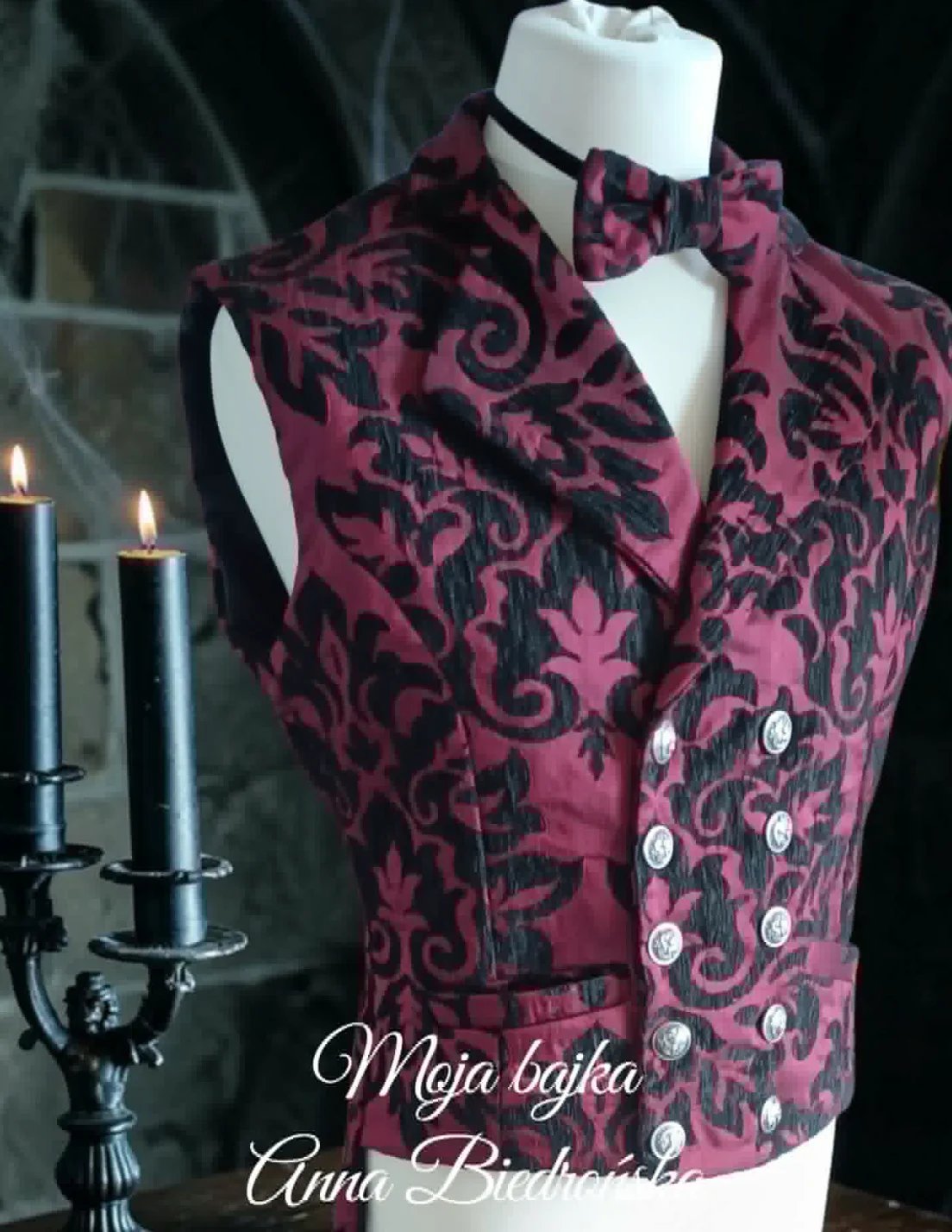 Burgundy damask patterned double-breasted vest with black bow tie on mannequin, styled with lit candles