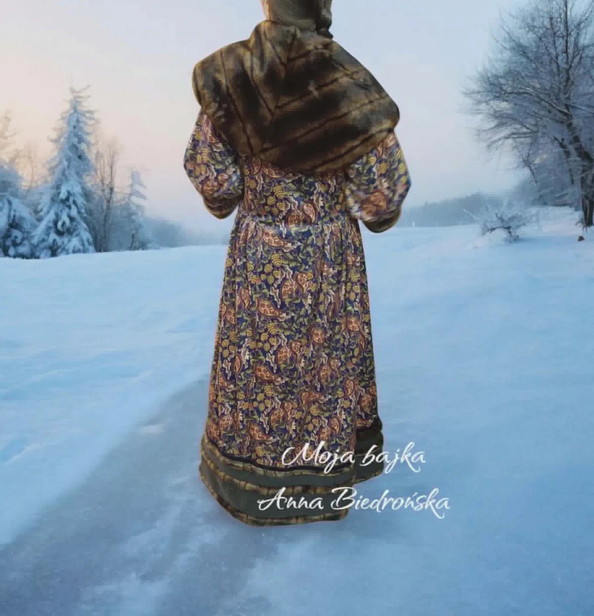 Woman in traditional patterned dress and fur wrap standing in snowy winter landscape with frosted trees