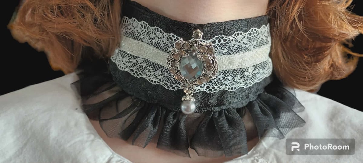 Person wearing ornate black lace choker with rhinestone brooch and tulle ruffle detail around the neck