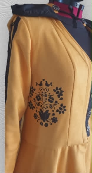 Yellow dress with black floral embroidery on the sleeve displayed on a hanger with other clothing items