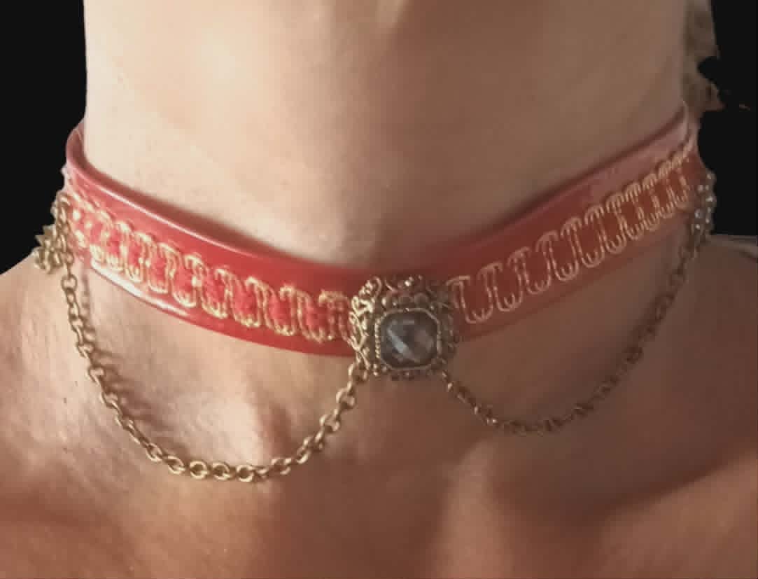 Person wearing a pink ribbon choker with decorative chain pendant around the neck