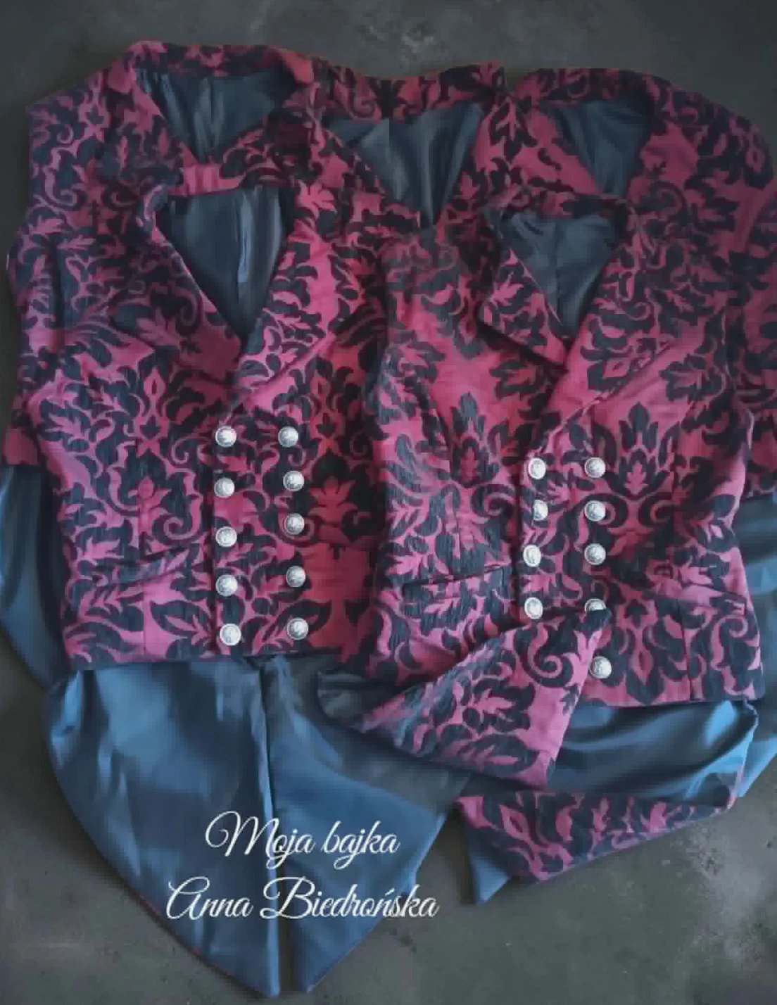 Pink and black ornate patterned jacket with pearl buttons displayed on blue fabric