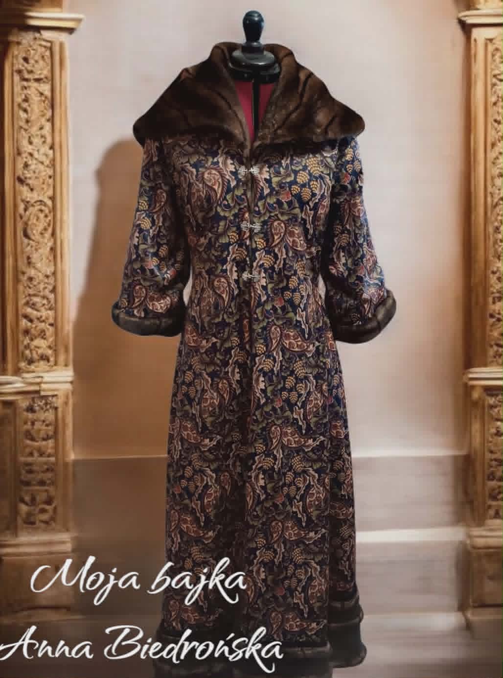 Vintage coat on mannequin with ornate brocade pattern, fur-trimmed collar and cuffs, displayed between decorative gold frames