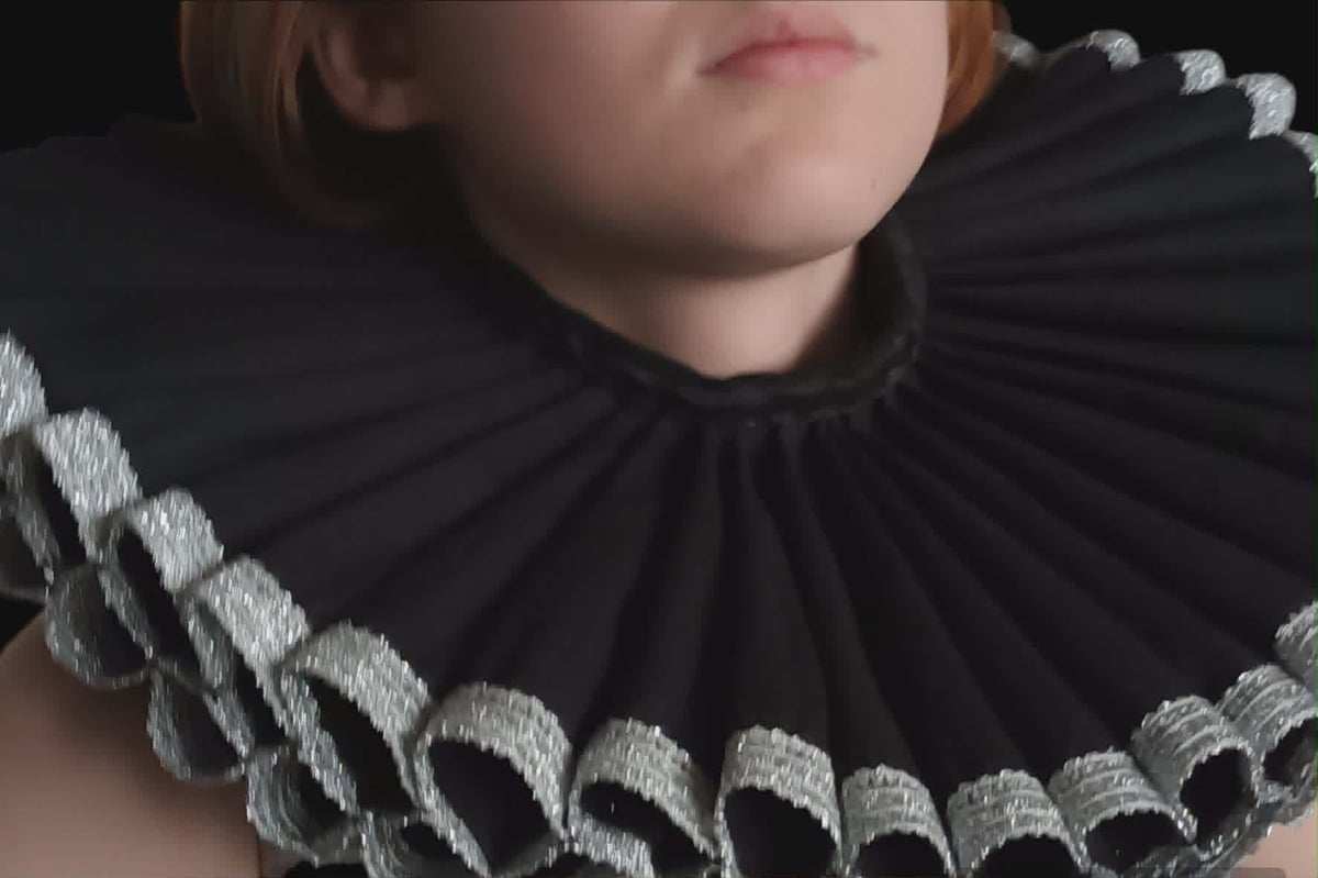 Close-up of a person wearing a black ruffled collar with silver embroidered trim