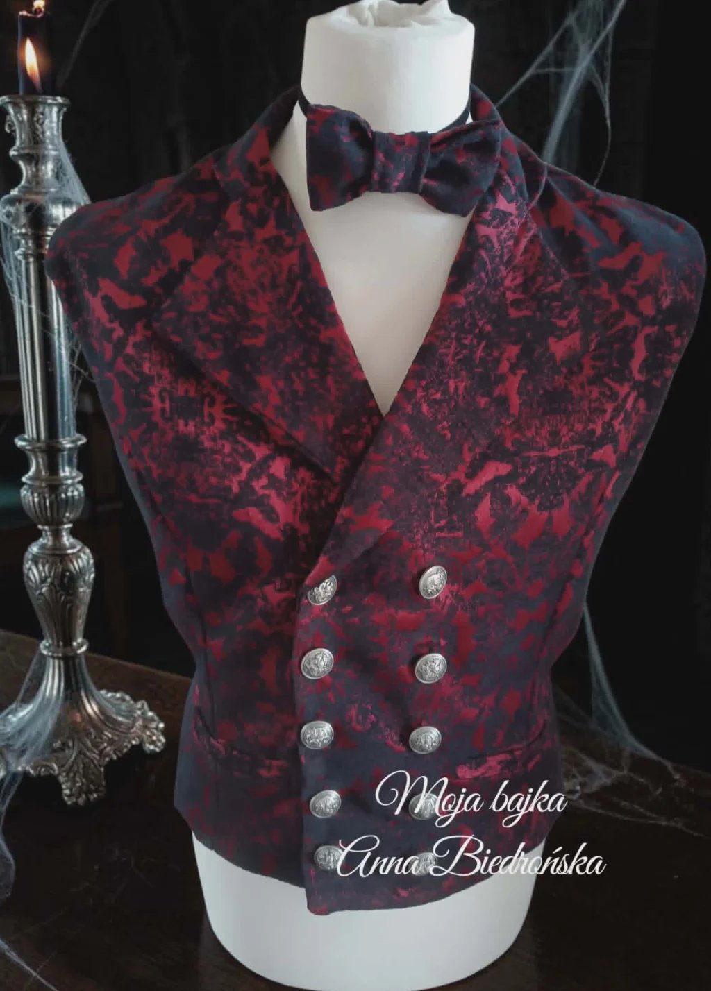 Red velvet double-breasted waistcoat with bow tie on dress form mannequin against dark background