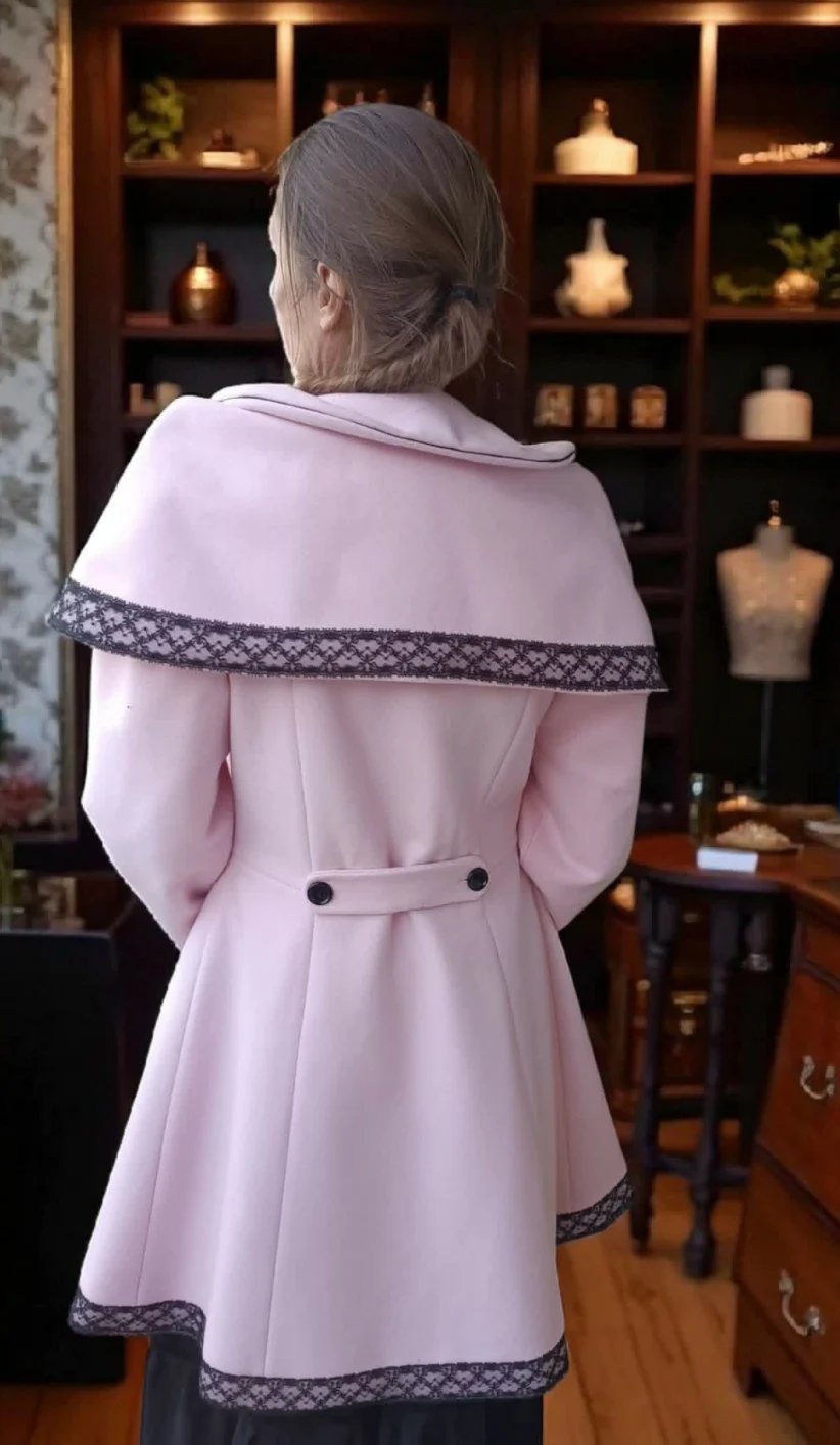 Woman viewed from behind wearing a pink coat with decorative trim, standing in a home interior with wooden shelving