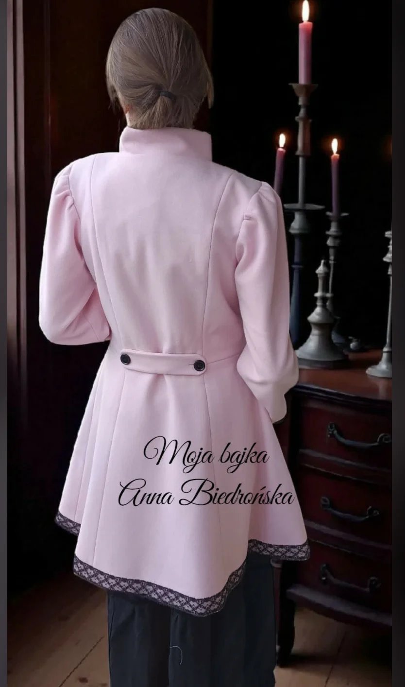 Woman from behind wearing pink cardigan over dark pants, standing before candlestick with lit candles in dim interior
