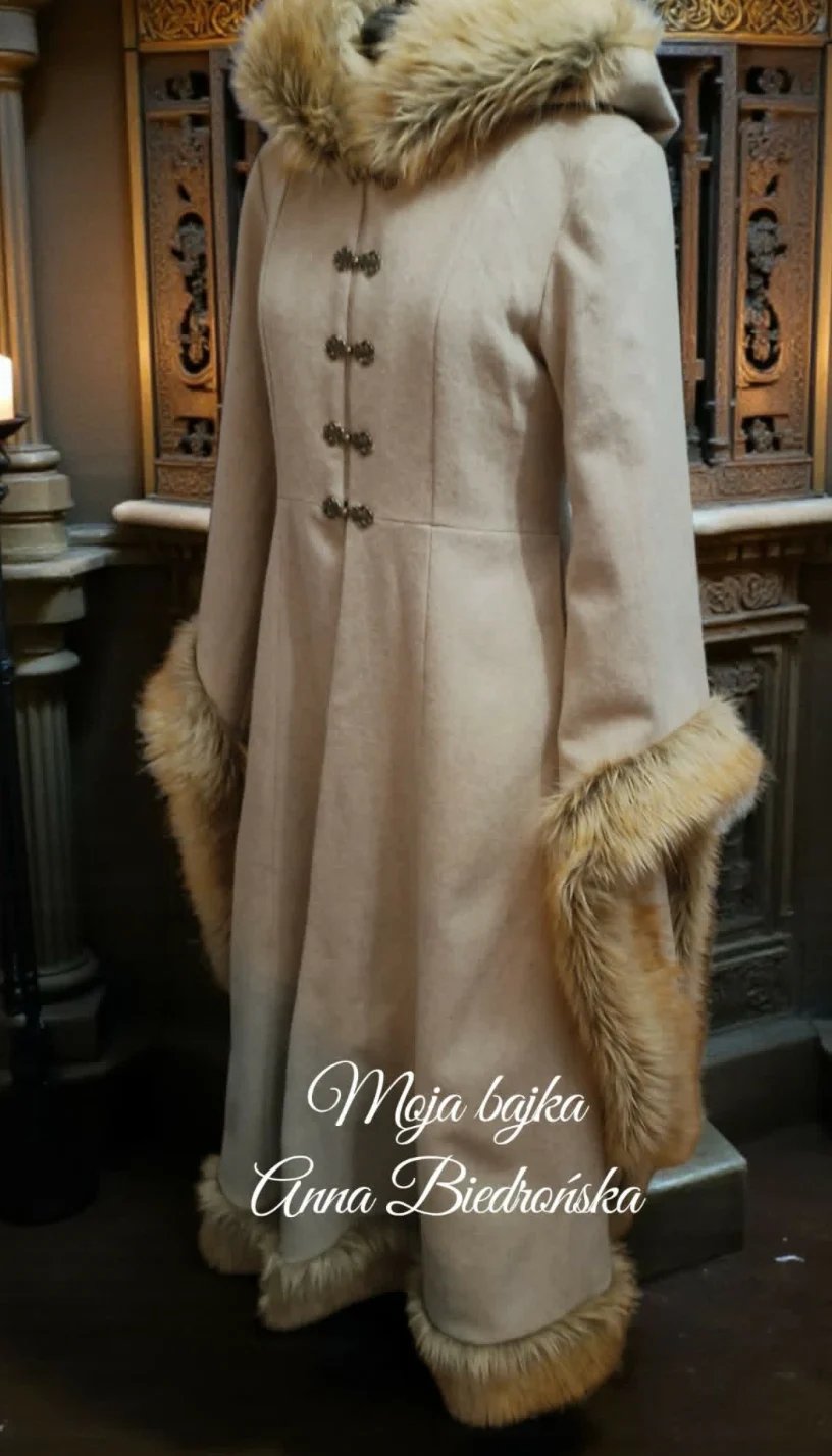 Cream-colored dress coat with fur collar and cuffs displayed on mannequin with ornate carved panels in background