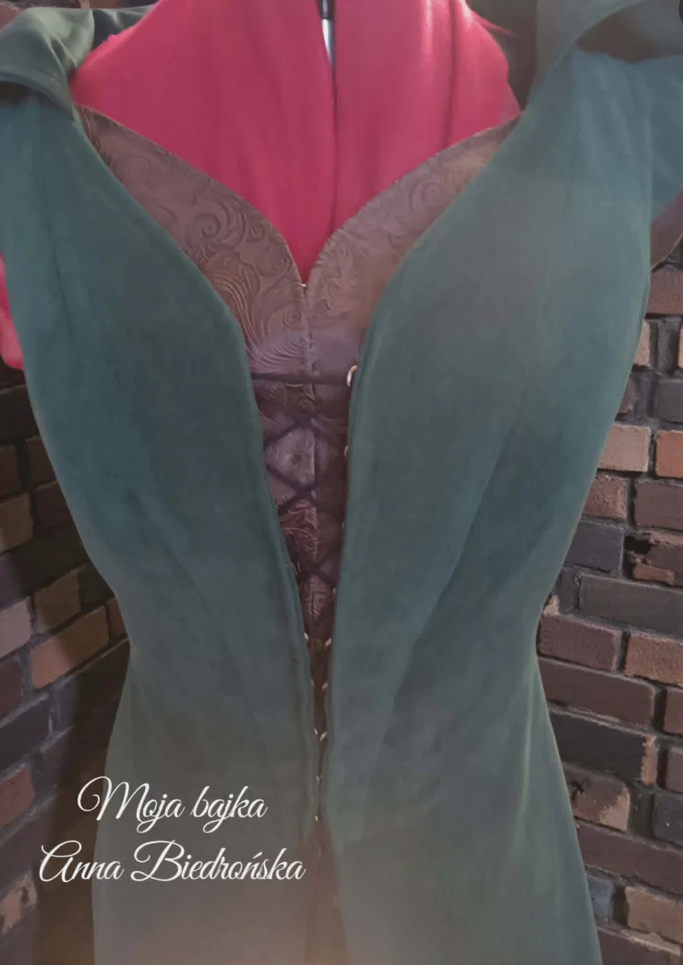 Turquoise robe with pink inner lining and ornate mauve panel detail displayed on brick background