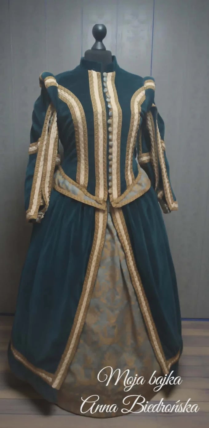 Historical period dress on mannequin featuring dark teal gown with cream and gold striped trim, displayed in museum setting