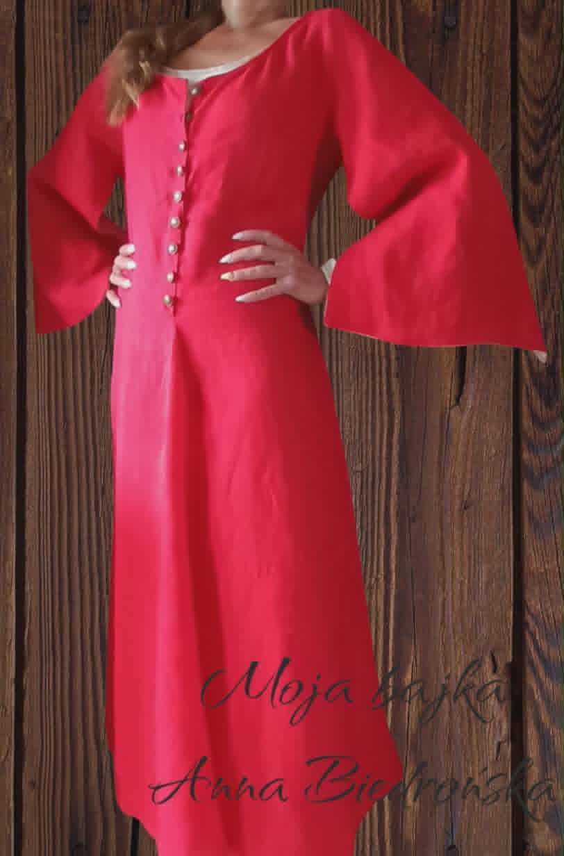 Woman wearing a red medieval-style tunic dress with bell sleeves and button front, standing against a wooden background
