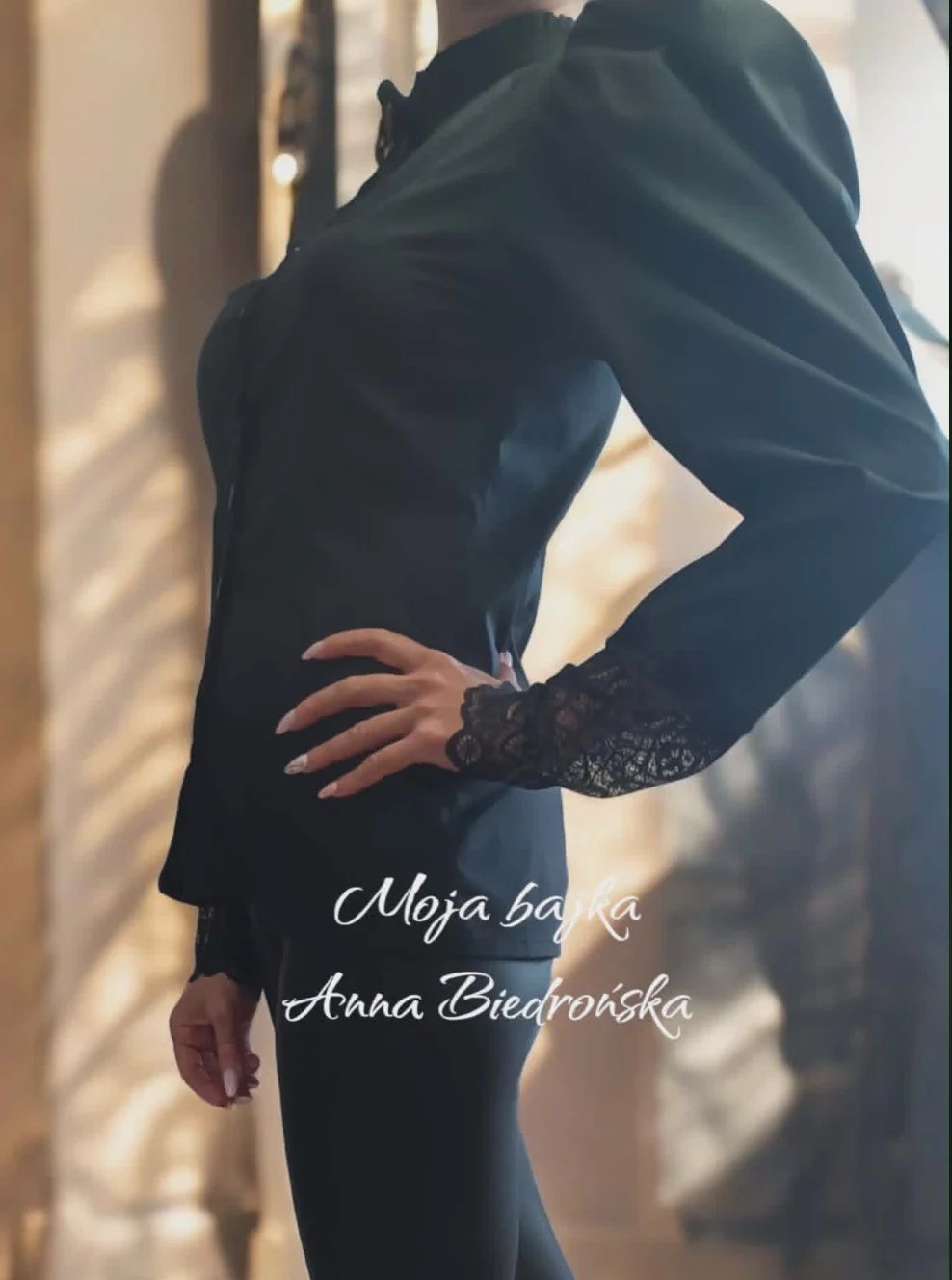 Woman in black lace dress posing against sunlit wall with credits for Moja baba and Anna Biedronska