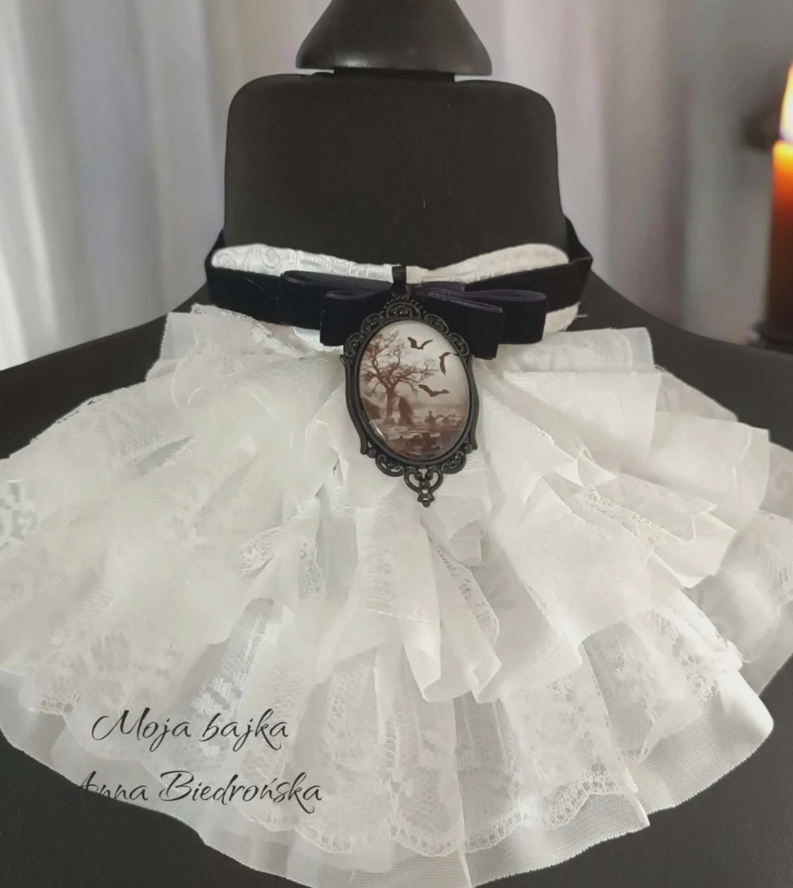 Black dress form displaying white lace collar with black ribbon and decorative cameo pendant