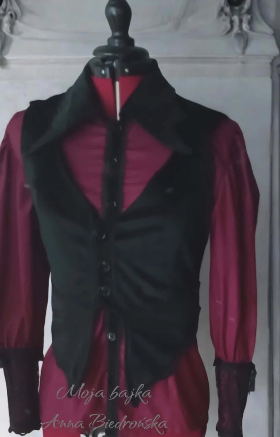 Mannequin displaying burgundy blouse with black vest and wide collar, styled outfit on dress form