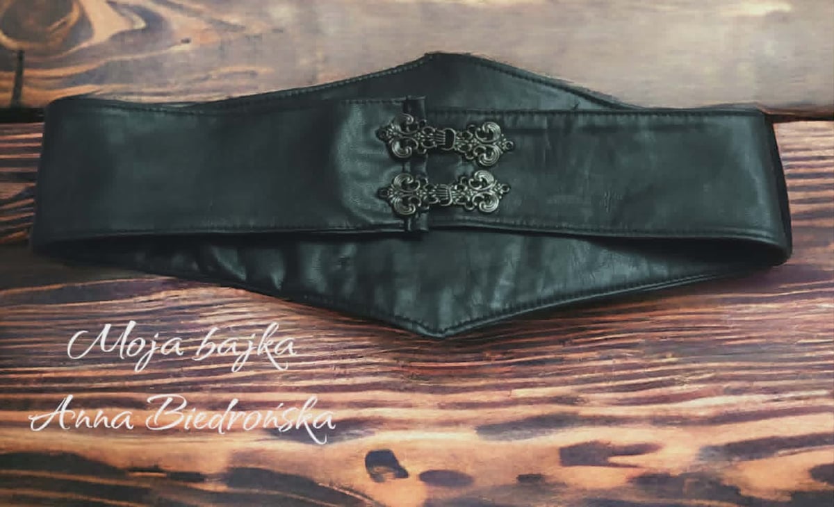 Green leather waist belt with decorative silver buckle displayed on wooden surface