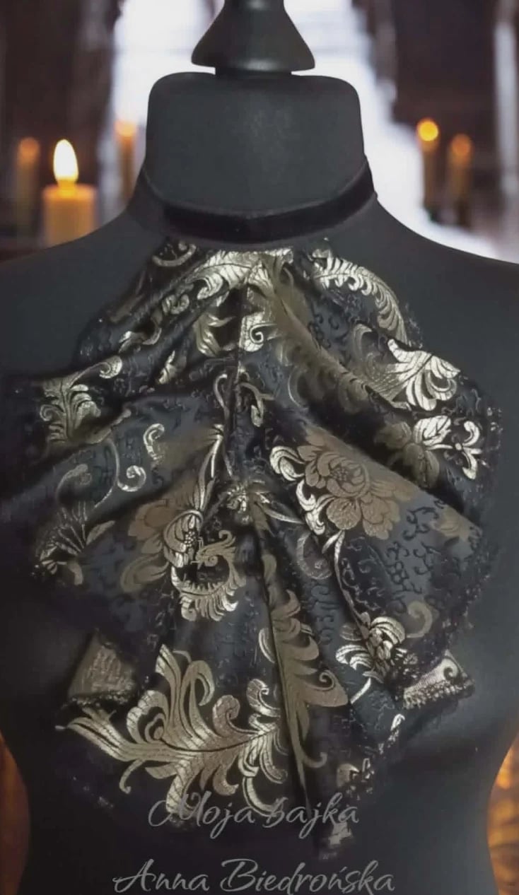 Black fabric mannequin displaying ornate cream and silver patterned fabric scarf in an elegant hallway with warm lighting