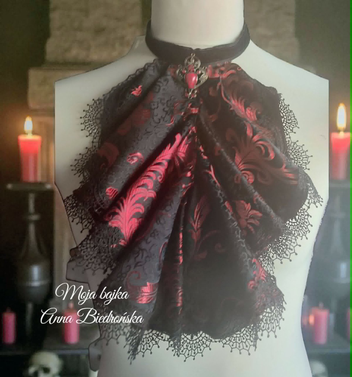 Gothic lace shawl with red and black floral patterns draped on a dress form, displayed with candles