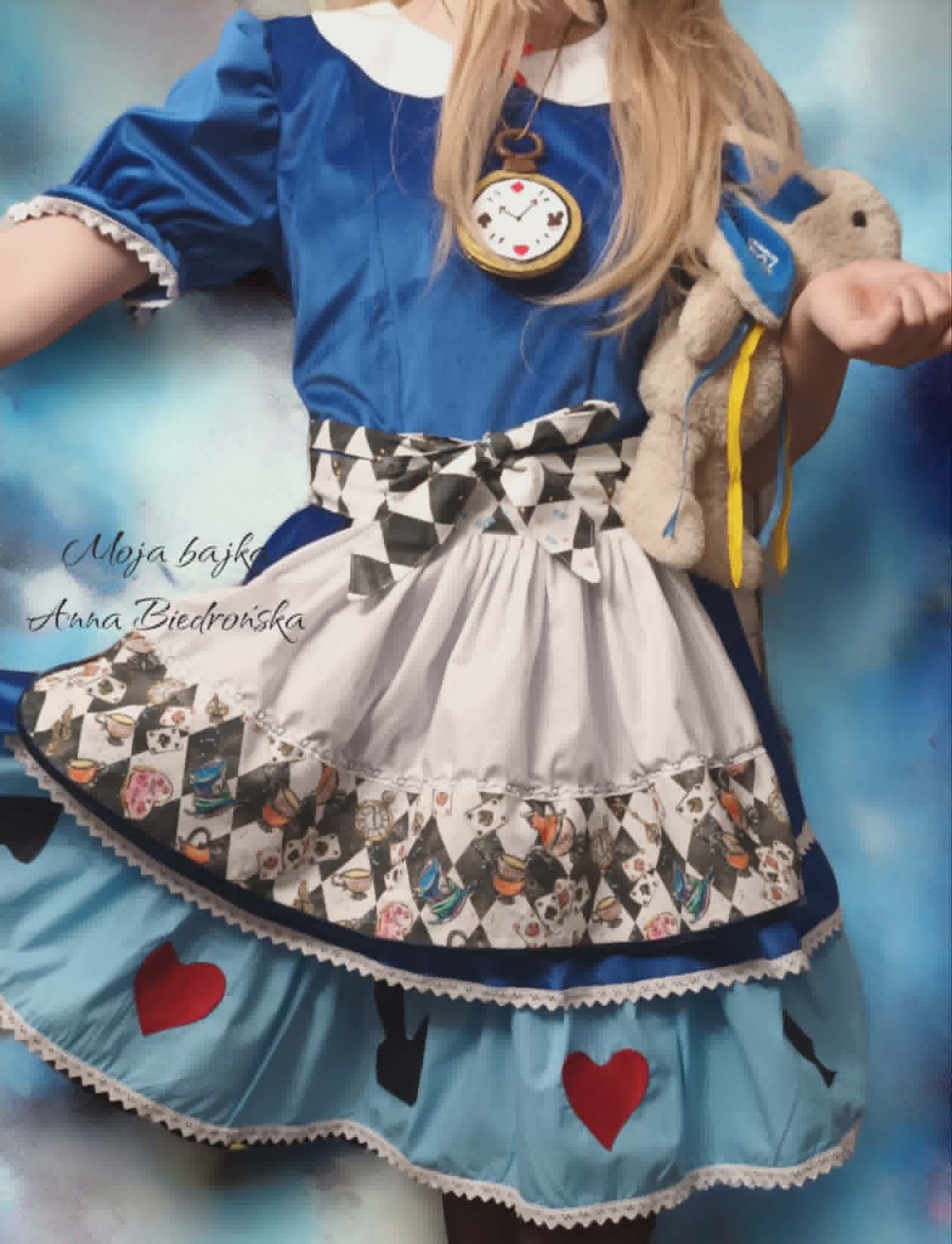 Girl wearing blue dress with layered skirt, pocket watch necklace, and striped bag against blue background