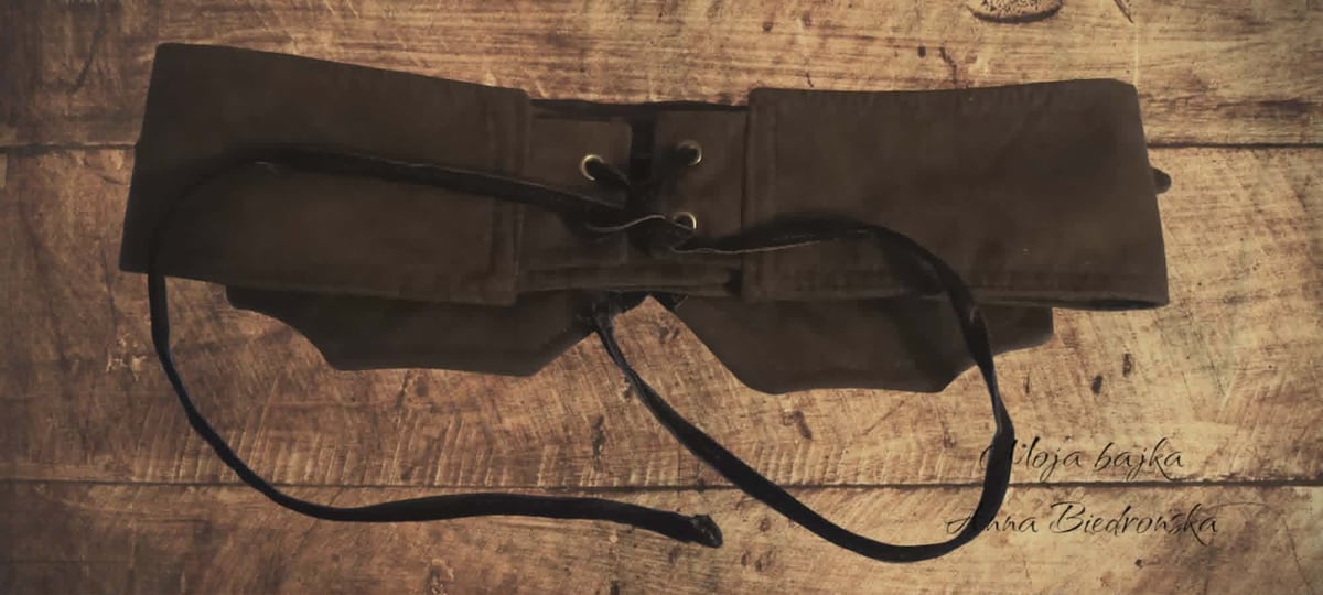 Black tool belt or apron with straps laid flat on a weathered wooden surface