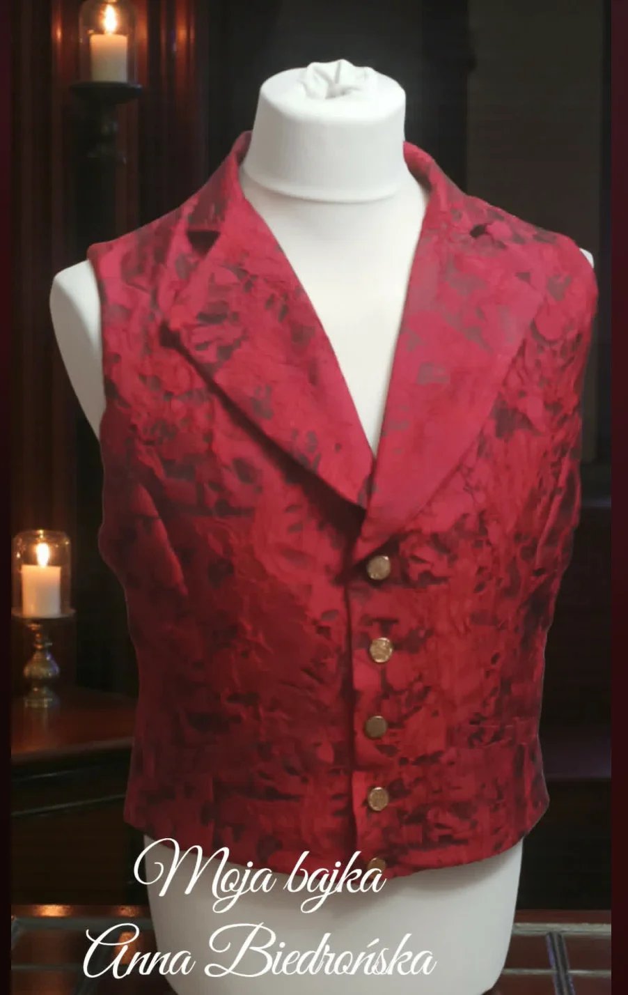 Red brocade vest displayed on a mannequin with candles in background, credited to Anna Biedhorska