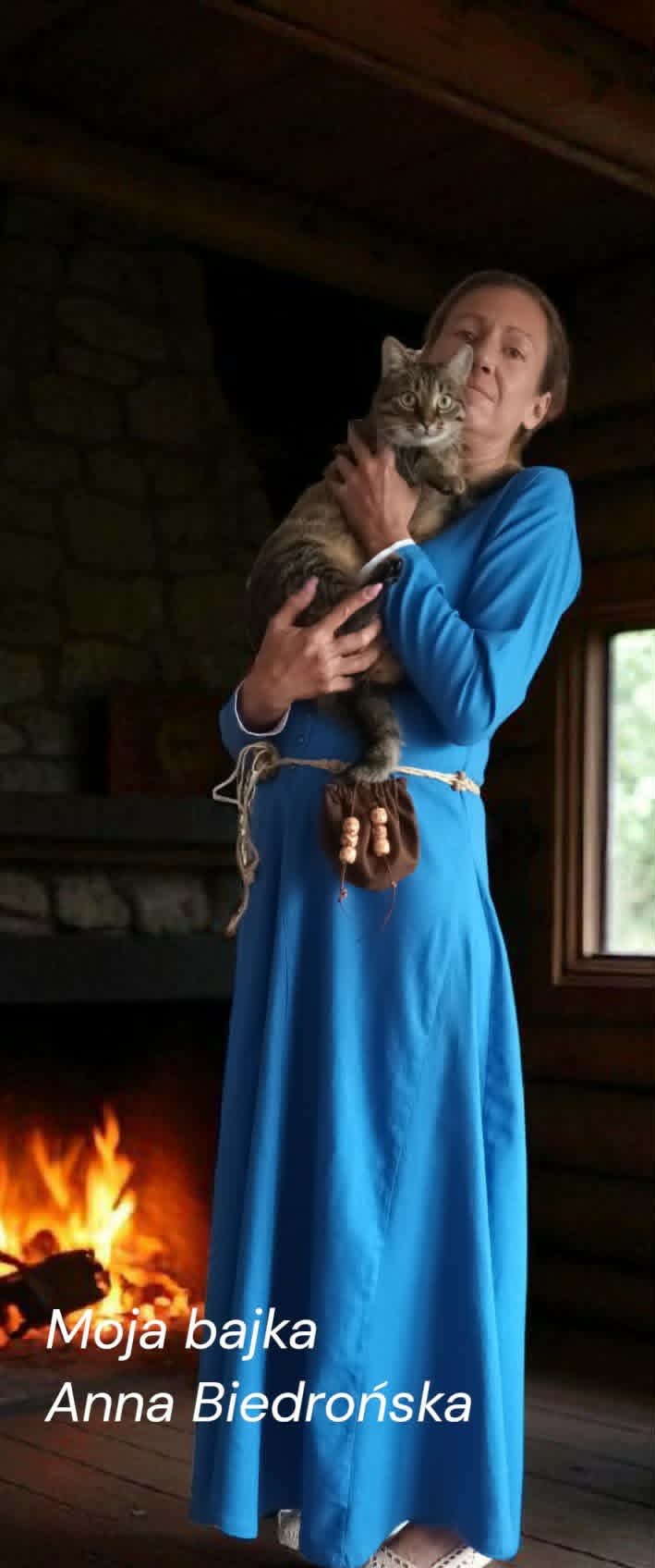 Woman in blue dress holding tabby kitten by fireplace indoors