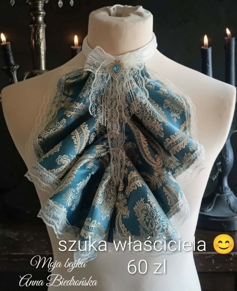 Ornate blue and gold bow tie with lace trim displayed on a white dress form, surrounded by lit candles