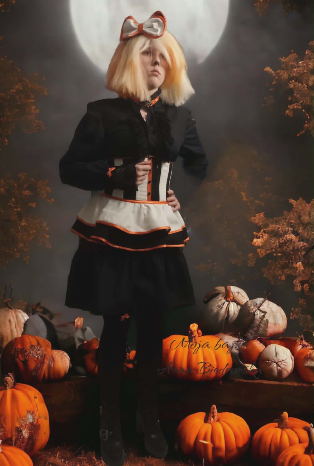 Young girl with blonde hair and red bow wearing black outfit standing among pumpkins under full moon