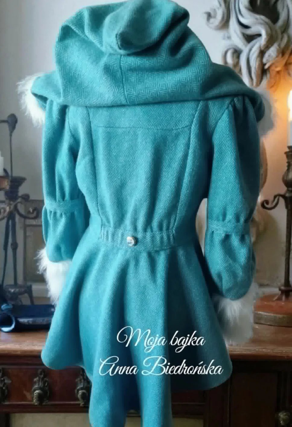 Turquoise wool coat displayed on a mannequin, featuring a cinched waist and fluffy white fur collar trim
