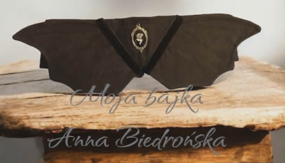 Black fabric bat-shaped decorative item displayed on a wooden log with watermarked text