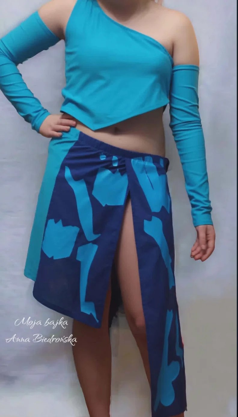 Woman wearing turquoise one-shoulder crop top with long sleeves and navy skirt with turquoise abstract pattern
