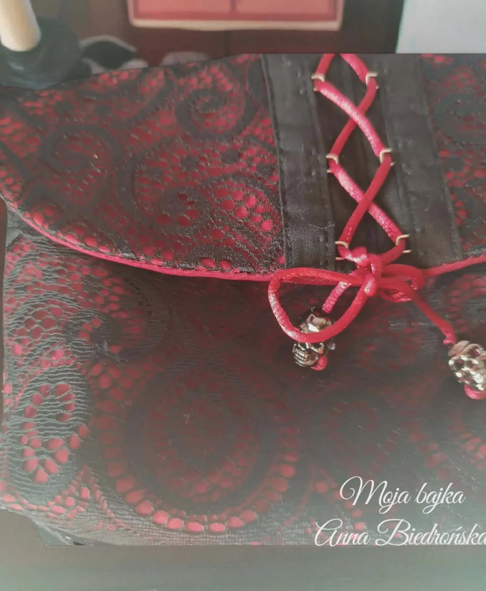 Red and black decorative fabric pouch with ornate damask pattern, pink cord closure, and silver charms hanging from drawstring