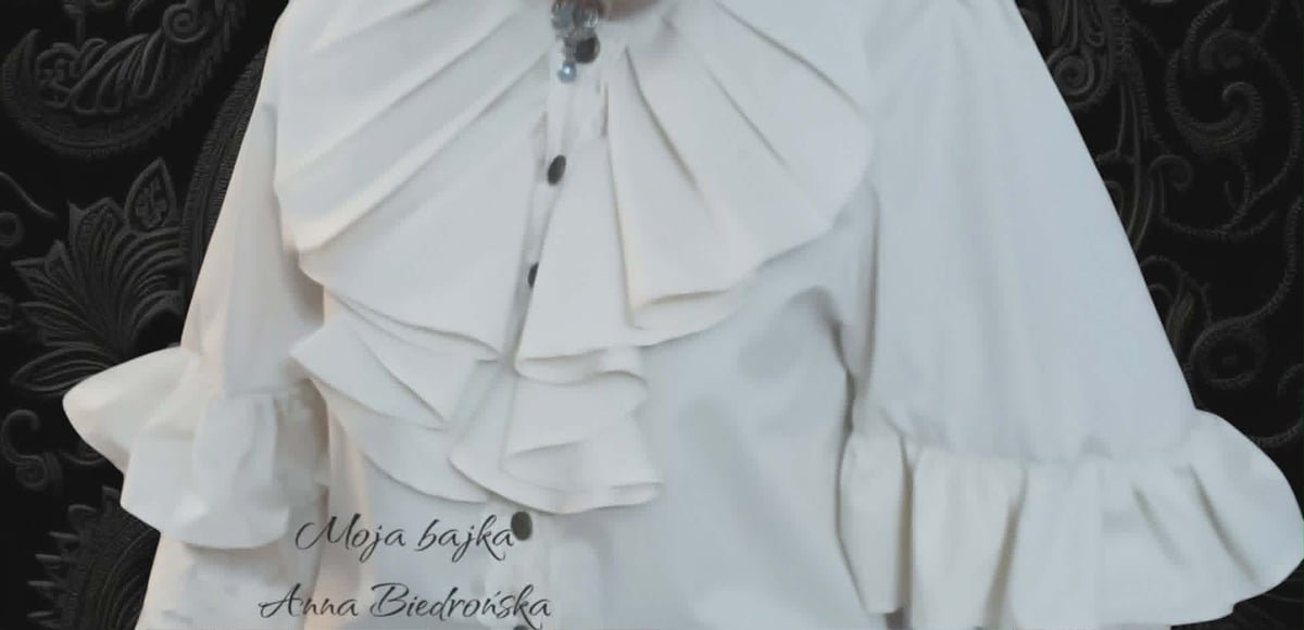 Close-up of a white ruffled blouse with layered fabric details and bell sleeves against a dark decorative background